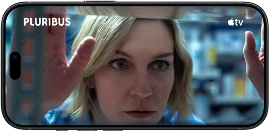 iPhone 18 Pro, landscape mode, displaying a close-up of a woman looking through shelves. Series title: Pluribus