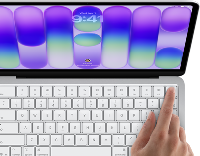 MacBook Neo, silver colour, showing login screen, person's finger on Touch ID sensor in top-right corner of keyboard